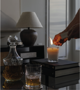 Lighting a Lēoht candle with a match beside a whiskey decanter